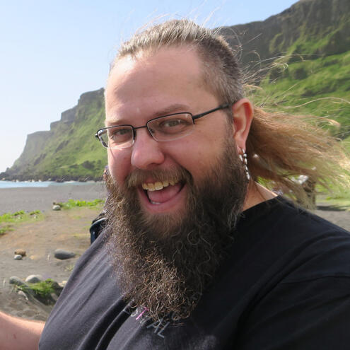 Josh's smiling face as he stands on the black sand beach of Iceland